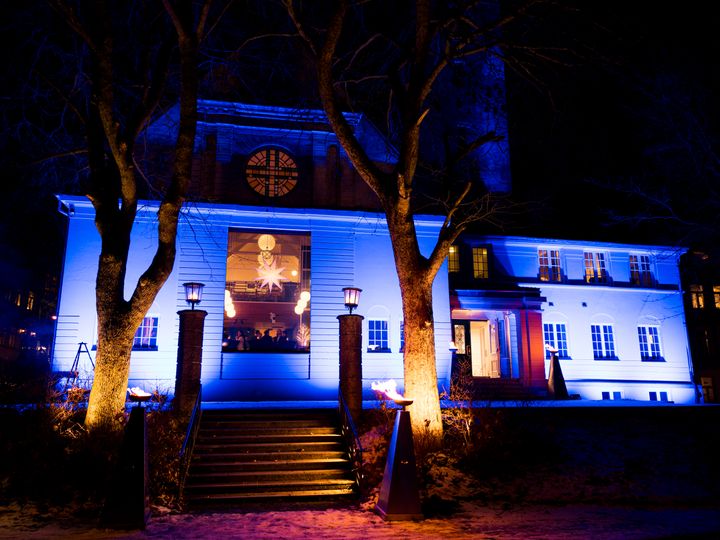 En fasade med trapp og innrammet av to store trær lyst opp i blått