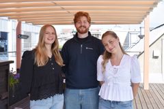 Tre personer står under en pergola, smiler til kameraet