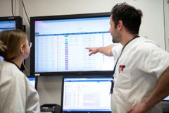 Bilde av to sykehusansatte som skjer på en stor skjerm