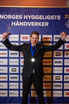 Bjørn Bakken står foran sponsorveggen og feirer med pokalen i hånda.