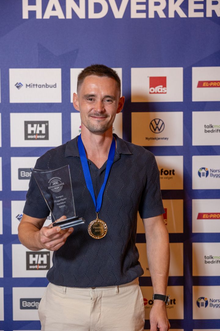 En smilende Hilmar Iversen står foran sponsorveggen med pokalen i hånda.