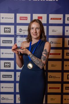 Ewelina Sekiw står foran sponsorvegg og viser frem pokal.