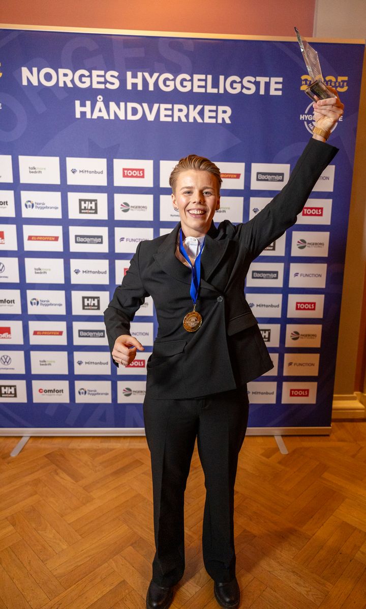 Thea Stornes står foran sponsorveggen og feirer at hun ble kåret til Norges Hyggeligste Lærling 2025.