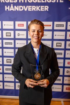 Thea Stornes står smilende foran sponsorveggen under kåringen av Norges Hyggeligste Håndverker 2025.