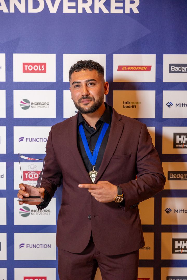 Sajjad Youssefi viser frem pokalen foran sponsorveggen under kåringen av Norges Hyggeligste Håndverker 2025.