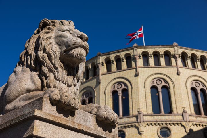 En av løvene på Løvebakken fotografert med deler av stortingsbygningen i bakgrunnen.