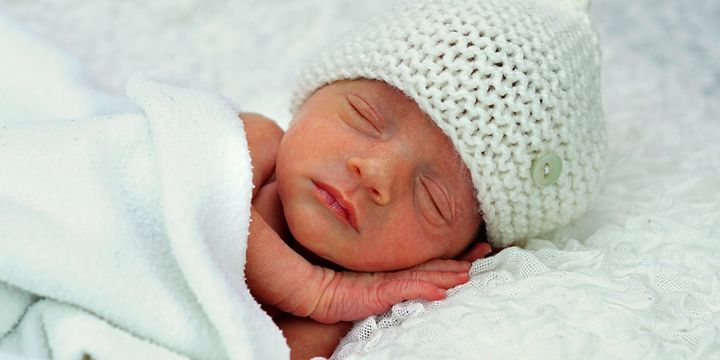 Bildet viser en for tidlig født baby som sover med hvit lue på