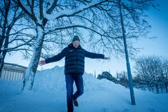 Mann med utslåtte armer som går ned fra en snøhaug. Kaldt vintervær