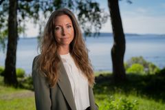 Portrettfoto av kvinne stående utendørs med grønt gress, trær og sjøen i bakgrunnen.