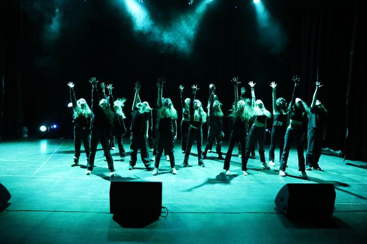 Bilde av flere ungdommer på en scene. Grønt scenelys skinner over dem og de har hendene i været