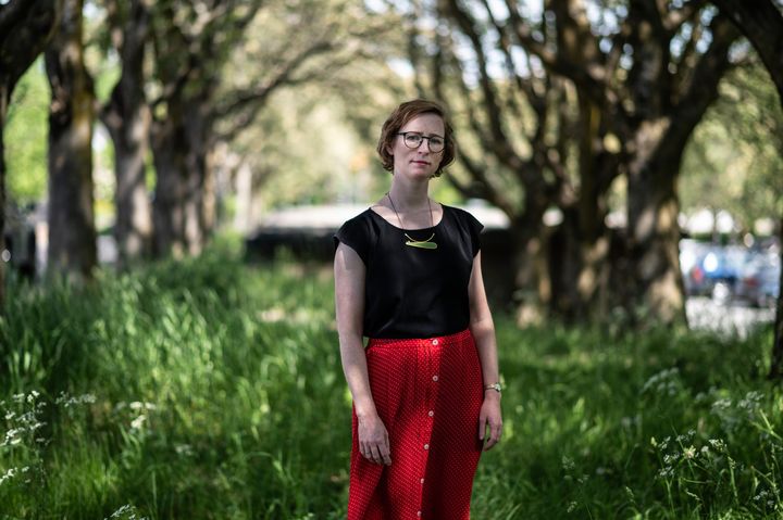 Kristine Garvin i rødt skjørt og sort t-skjorte står under en allè av trær på grønt gress.
