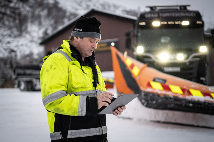 Bildet viser at brøytebilsjåføren sjekker vær- og farevarsler på Værio foran brøytebilen sin ute i snøen.