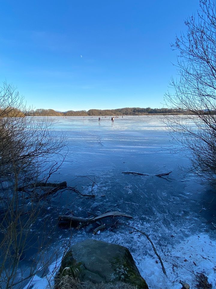 Is på stort vann, skøytende barn og voksne, klar himmel.