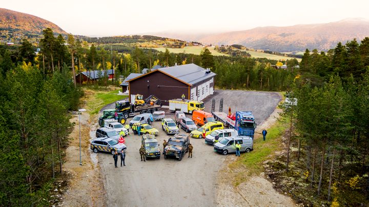 Kjøretøy fra ulike deler av totalforsvaret samlet foran en stor garasje.