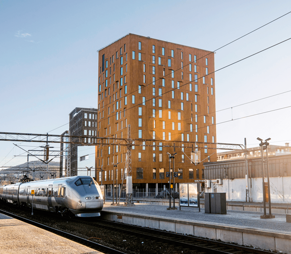 Illustrasjonsfoto: Høye kontorbygg sett fra perrongen på en togstasjon. Tog står ved perrongen nærmeste kontorbygningene.