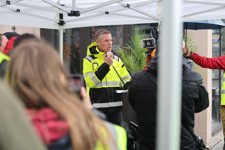 En person i gul refleksjakke holder en tale under en støttemarkering.