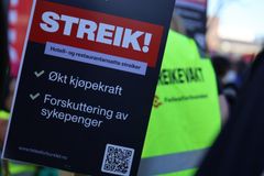 Skilt med teksten "Streik! Hotell- og restaurantansatte streiker. Økt kjøpekraft. Forskuttering av sykepenger." Personer med gule vester i bakgrunnen.