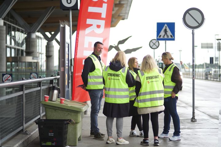 Ansatte med gule vester står sammen under streik ved en flyplass.