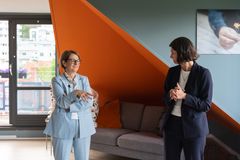 To personer står og snakker i en stue med moderne innredning.