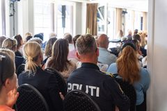 Publikum med en politibetjent sitter i et fullt lokale under et arrangement.
