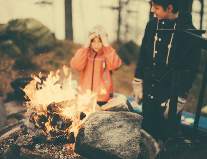 Bildet er av to barn som står ved et brennende bål i skogen.