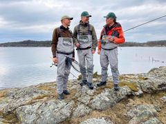 De tre deltakerne i Jakt- og fiskepodden om står ved vannkanten med fiskeutstyr.