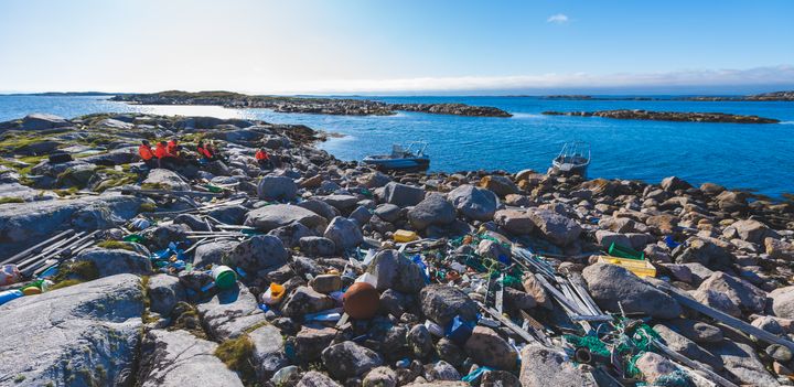 Plast som ligg i fjæresteinane ut mot havet. Personar i bakgrunn.