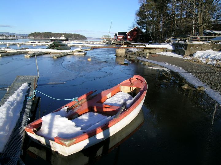 Gammel og delvis ødelagt jolle ligger fortøyd i småbåthavn.