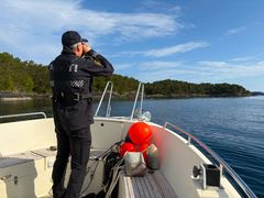 Politimann speider utover sjøen fra båt.