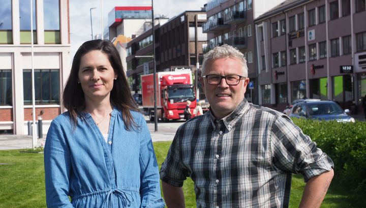 To personer står foran en grønn plen med bygninger