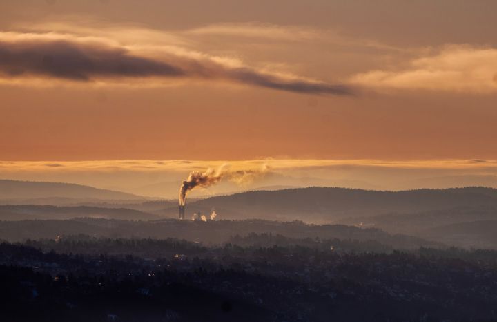 Landskap i dis og orange lys med fabrikkpipe som slipper ut røyk i det fjerne