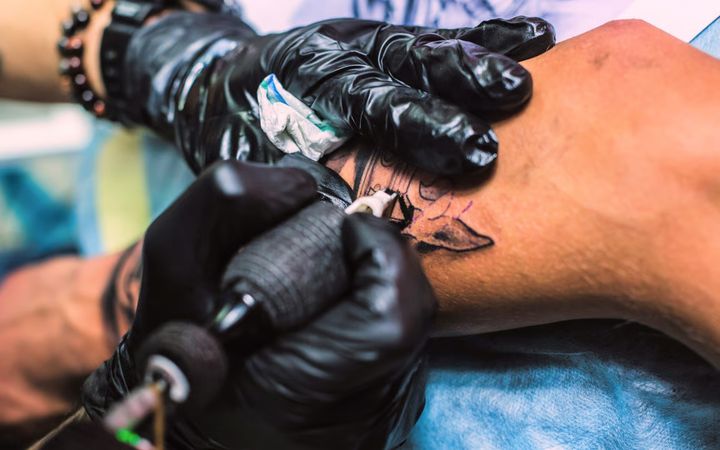 To hender som tatoverer en person like under kneet.