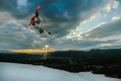 En snowboardkjører gjør et akrobatisk hopp i solnedgangen over et snødekt landskap.