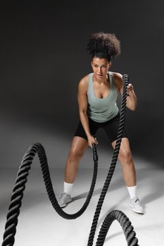 En kvinne trener med battle ropes i et studio.