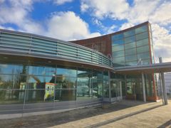 Fasaden til en ny XXL-butikk i handelsområdet Tiiriö i Hämeenlinna, Finland, med store glassvinduer og blå himmel med skyer.