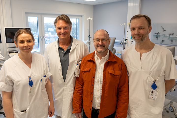 En kvinnelig sykepleier, mannlig lege, pasient (voksen mann med oransje jakke og briller) og mannlig kirurg står i et behandlingsrom på sykehus.