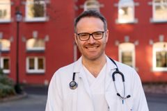 mann i legefrakk smiler