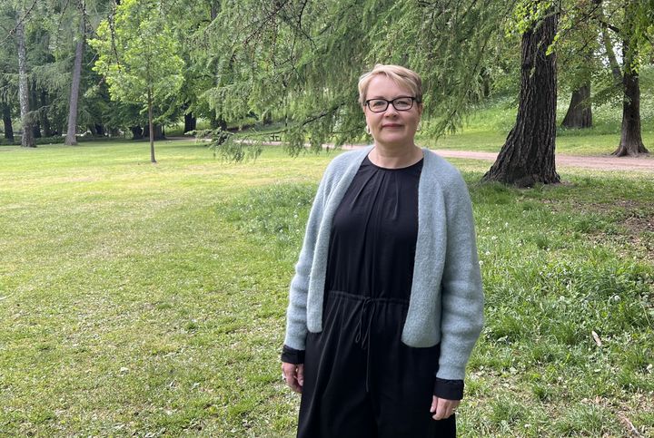 Portrett av den finske sosiologen Suvi Salmenniemi i svart kjole med grønne trær i bakgrunnen