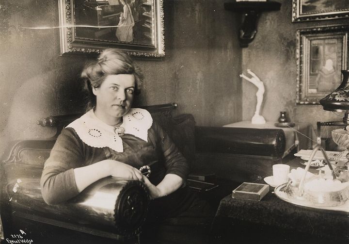 Marie Hamsun sitter i en sofa med en kopp kaffe på bordet foran seg.