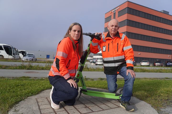 To ansatte i Statens vegvesen som holder en el-sparkesykkel mellom seg, med hovedkontoret for Statens vegvesen i bakgrunnen.