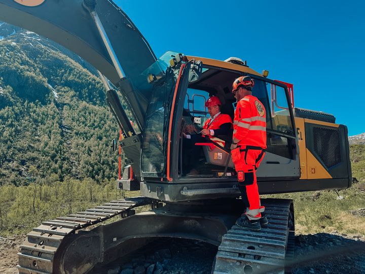 Bilde av samferdselsministeren inni en gravemaskin sammen med en som jobber i Bertelsen og Garpestad