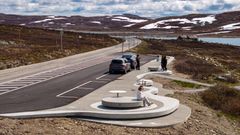 To ungjenter sit på runde rastemøblar i betong og ser på utsikta over innsjøen Ørteren på Hardangervidda. Nokre turistar tek bilete av kvarandre i bakgrunnen.