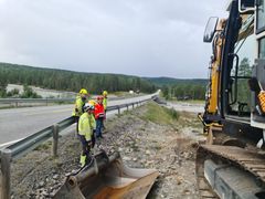 Bildet viser arbeidsfolk som står ved en gravemaskin på siden av dagens E45. Bildeteksten sier, Forlenges: Fra eksiterende kraftnett videreføres kraften i kabel opp til anleggsområdet. Arbeidet startet ved Garajokka, på Altasiden av Kløfta.
