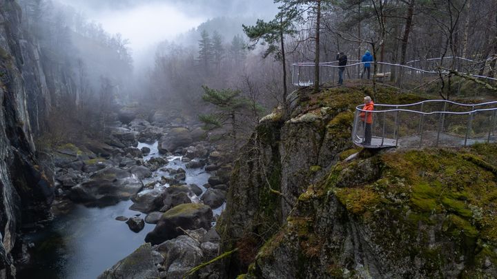 Tre menneske står på to ulike utsiktspunkt og ser ned på elveløpet.