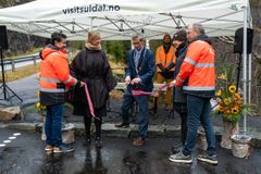 To kvinner og fire menn står samla. Varaordføraren i midten kuttar eit band.