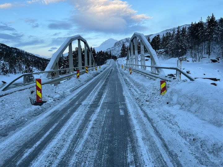 Buebru i stål på vinterveg med refleksstolper i forgrunnen.
