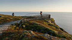 Illustrasjon av et utsiktspunkt på en fjellknaus med rekkverk, med havet i bakgrunnen og personer som oppholder seg på området.