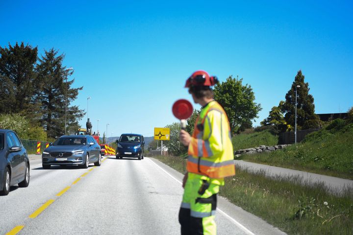 Foto av trafikkdirigent som stopper trafikk en sommerdag på veg.