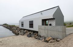 Et langstrakt servicebygg med sølvfarget kledning etablert i strandsonen ved Ersfjordstranda på Senja.