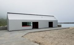 Et langstrakt servicebygg med sølvfarget kledning etablert i strandsonen ved Ersfjordstranda på Senja.